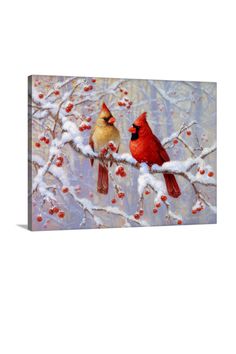 two cardinals perched on a snowy branch with berries in the foreground and one cardinal looking at each other