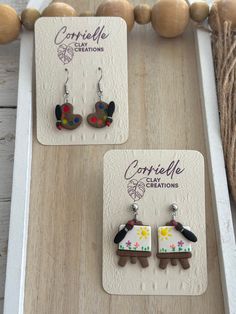 two pairs of earrings with designs on them sitting on a wooden table next to some balls