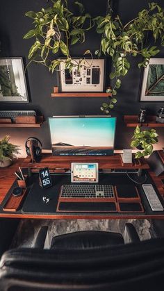 a desk with a computer, keyboard and plant on it in front of a black wall