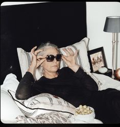 an older woman laying in bed with her eyes closed and holding up two glasses to her face