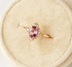 a pink diamond ring sitting on top of a white cushion