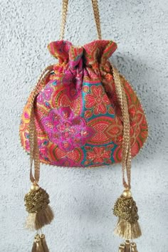 an orange and pink purse hanging on the wall with tassels attached to it