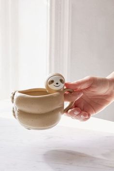 a hand holding a cup with a slot in it and a small doll inside the cup