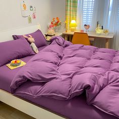 a bed with purple sheets and pillows in a room