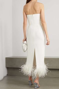 the back of a woman wearing a white dress with feathers on it