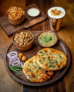 a wooden plate topped with food next to two bowls filled with different types of sauces