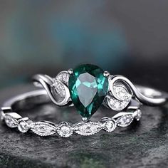 a green heart shaped ring sitting on top of a black rock with diamonds around it