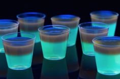 several shot glasses sitting on top of a table with blue and green liquid in them