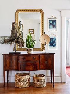 an antique burlwood sideboard in the entryway is beautifully balanced by a simple mirror, woven baskets, and original art