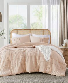 a bed with pink comforter and pillows in a room next to a wicker basket