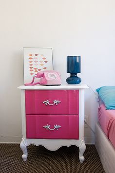 a pink and white dresser in a bedroom next to a bed with a blue pillow