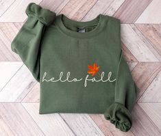 Celebrate your favorite season, Fall, with this moss olive green Hello Fall sweatshirt.  Welcome sweater weather and get cozy with warm apple cider in hand in this cute sweater. This sweater is made from polyester and cotton. This combination helps designs come out looking fresh and beautiful.  The collar is ribbed knit, so it retains its shape even after washing.   Knit in one piece using tubular knit, it reduces fabric waste and makes the garment more attractive.  There are no itchy side seams Olive Crew Neck Top For Winter, Khaki Cotton T-shirt For Fall, Fall Olive Crew Neck Top, Olive Crew Neck Top For Fall, Khaki Relaxed Fit Sweatshirt For Fall, Green Cotton Tops For Fall, Fall Khaki Cotton T-shirt, Khaki Crew Neck Sweatshirt For Fall, Khaki Crew Neck Tops For Fall