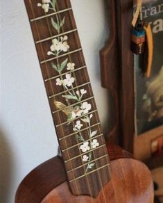 a ukulele with flowers and leaves painted on the fretboard is sitting in front of a wall