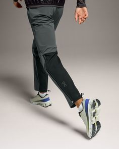 a man in black jacket and grey pants walking with foot on white skateboard against gray background