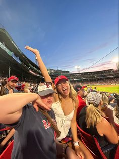 two women are sitting in the stands at a baseball game and one woman is raising her arm up