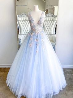 Daintily crafted, this stunning blue prom dress is the epitome of fairy-tale elegance. The dress features a deep V-neckline adorned with delicate floral appliques, adding a touch of romance and sophistication. The fitted bodice flows into a voluminous tulle skirt, creating a breathtaking silhouette that moves gracefully with every step. The pastel blue color and intricate details make this dress perfect for those who want to make a memorable entrance. Ideal for prom or any formal event, this gown ensures you will look and feel like a princess. Blue Long Prom Dress, Black Prom Dress Short, Tiara Hair, Prom Dress Plus Size, Dress With Embroidery, V Neck Prom Dresses, Golden Crown, Prom Designs, Blue Tulle