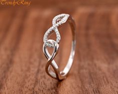 a white gold ring with an intertwined design on top of a wooden surface,