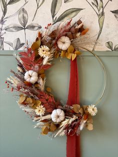 a wreath made out of dried flowers and leaves on a door frame with a red ribbon