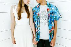 a young man and woman holding hands standing next to each other in front of a white wall