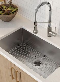 a stainless steel kitchen sink and faucet in a white countertop with wooden cabinets