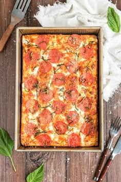 a square pizza sitting on top of a wooden table next to a knife and fork