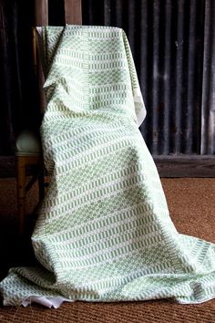 a green and white blanket sitting on top of a wooden chair next to a wall