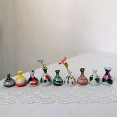 seven small vases are lined up on a white tablecloth, with one flower in the middle