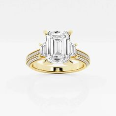 an emerald cut diamond engagement ring with two side stones on the band and shoulders, set in yellow gold