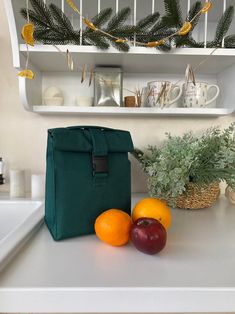 two oranges and an apple sit on the counter in front of a green bag