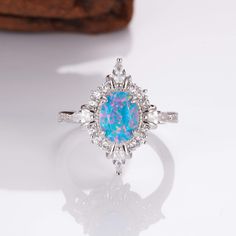 Mesmerizing Fire in Sterling Silver: Mia Ring. This handcrafted ring features a captivating natural blue fire opal, its brilliance flickering with every move. A timeless treasure that adds a touch of magic to any outfit (sizes 3.5-14.25). ✦ DETAILS ✦ ✧ Handcrafted  ✧ Fire opal and natural crystals  ✧ Sizes 3.75-14.25 ✧ This ring  will arrive ready to gift in a Kherish Jewelry Pouch. ✧ Due to the nature of the handmade process, each piece may slightly vary in color, size, shape, and contain natur Opal Ring With Center Stone As Gift, Opal Ring With Center Stone For Gift, Opal Halo Jewelry As Gift, Opal Rings With Halo Setting As A Gift, Opal Jewelry With Halo Setting For Gift, Blue Opal Ring For Gift, Fine Jewelry Style, Blue Opal Ring For Gift In Fine Jewelry Style, Blue Opal Promise Ring, Opal Ring With Halo Design For Gift