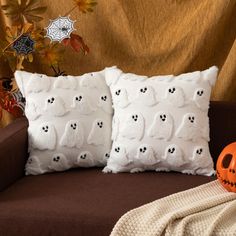 two decorative pillows on a couch with a pumpkin and spider webs in the background