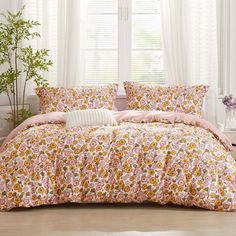 a bed with pink and yellow flowers on it in front of a white curtained window