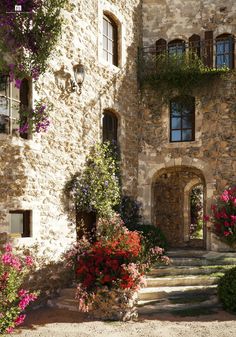 an old stone building with flowers growing out of the windows and steps leading to it