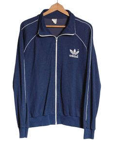 Vintage Adidas Europa track jacket in a navy blue colour. This is an original from the 1970's. Trademark three stripes down the sleeves with large trefoil on the chest. Elasticated waist and cuffs. Made in Thailand from a cotton nylon blend. Label reads GB 6'1". Condition: Excellent vintage condition. Chest: 44in Length: 26in Inside sleeve: 19in More vintage clothing on our website www.brickvintage.com Vintage Adidas Jacket, Blue Track Jacket, Jacket Adidas, Adidas Vintage, Vintage Adidas, Navy Blue Color, Blue Colour, Track Jacket, Track Jackets