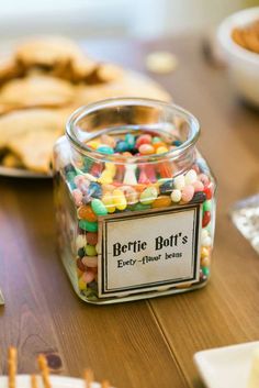 a jar filled with lots of candy sitting on top of a table next to cookies