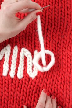 someone is knitting the letters on a red sweater