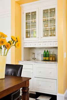 a kitchen with white cabinets and yellow flowers in a vase on top of the counter