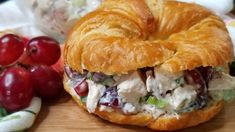 a croissant sandwich with chicken salad on it next to grapes and cherries