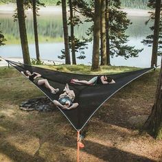 two people laying in a hammock on the ground near trees and water,