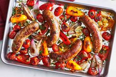 sausages, tomatoes and onions on a baking pan with herbs in the middle to cook