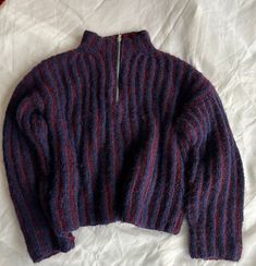 a red and blue striped sweater laying on top of a white sheeted bed spread