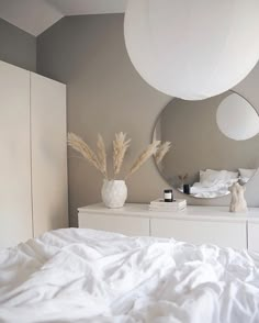 a bed with white sheets and pillows in a bedroom next to a large round mirror