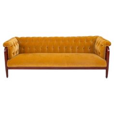 an orange velvet couch with wooden legs and buttons on the back, against a white background