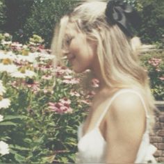 a woman standing in front of flowers with long blonde hair wearing a black bow on her head