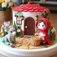 a little red riding hood on top of a cake with animals around it and a house in the background