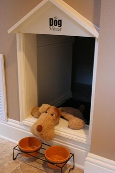 a dog house with two bowls and a stuffed animal on the ledge next to it