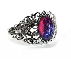 This bracelet is stunning! The focal point of this Victorian style bracelet is the 18x25 oval glass cabochon which has been made in the style of a Mexican Opal also known as Dragon's Breath (made from glass not a gemstone). With each slight turn, the colors shift from deep scarlet red to lightening strikes of blues!  Available in 6 Metal Finishes: Gunmetal Black, Antique Silver, Bright Silver, Antique Gold, Rose Gold or Antique Pewter. Please see photos for samples of each and make your selectio Dragons Jewelry, Opal Cuff Bracelet, Bracelet Mexican, Opal Bangle, Jelly Opal, Mexican Opal, Filigree Bracelet, Dragons Breath, Mexican Fire Opal