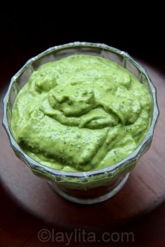 a glass bowl filled with green guacamole on top of a wooden table