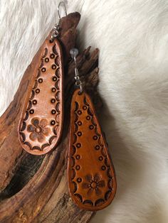 two wooden earrings are sitting on a piece of driftwood with white fur in the background