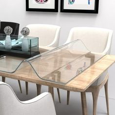 a glass table with white chairs in front of two framed pictures on the wall behind it